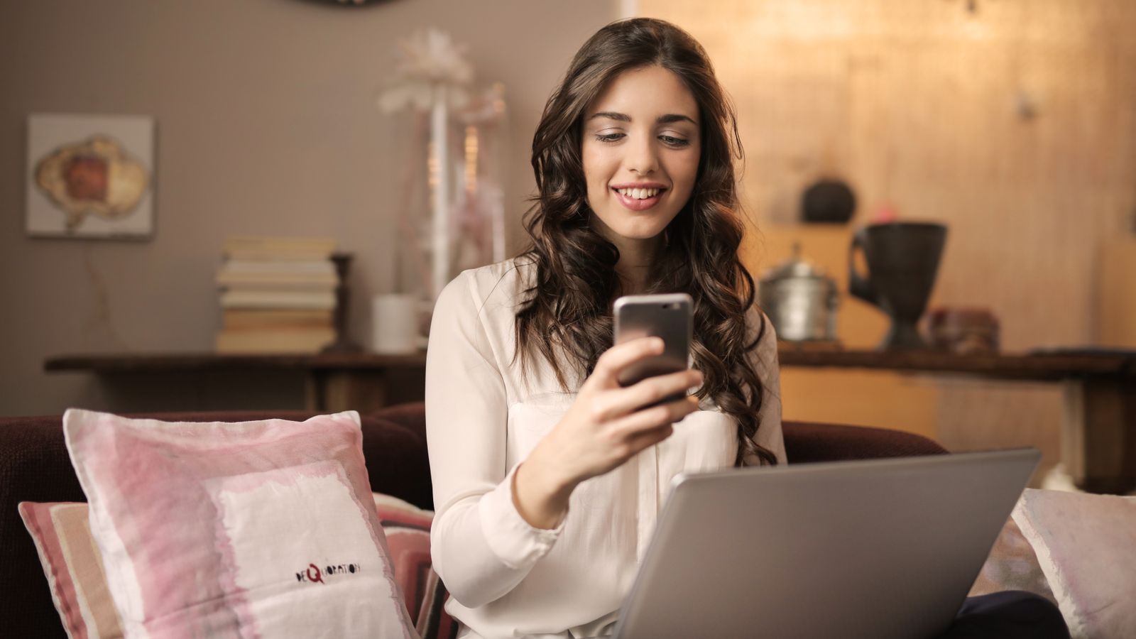 Woman choosing photos on her phone with a laptop nearby, planning a digital scrapbooking app project