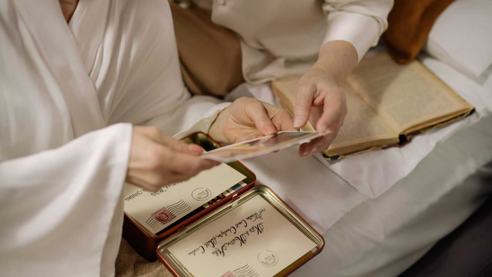 Two people passing an old photograph between them while building a family history scrapbook from a tin of letters
