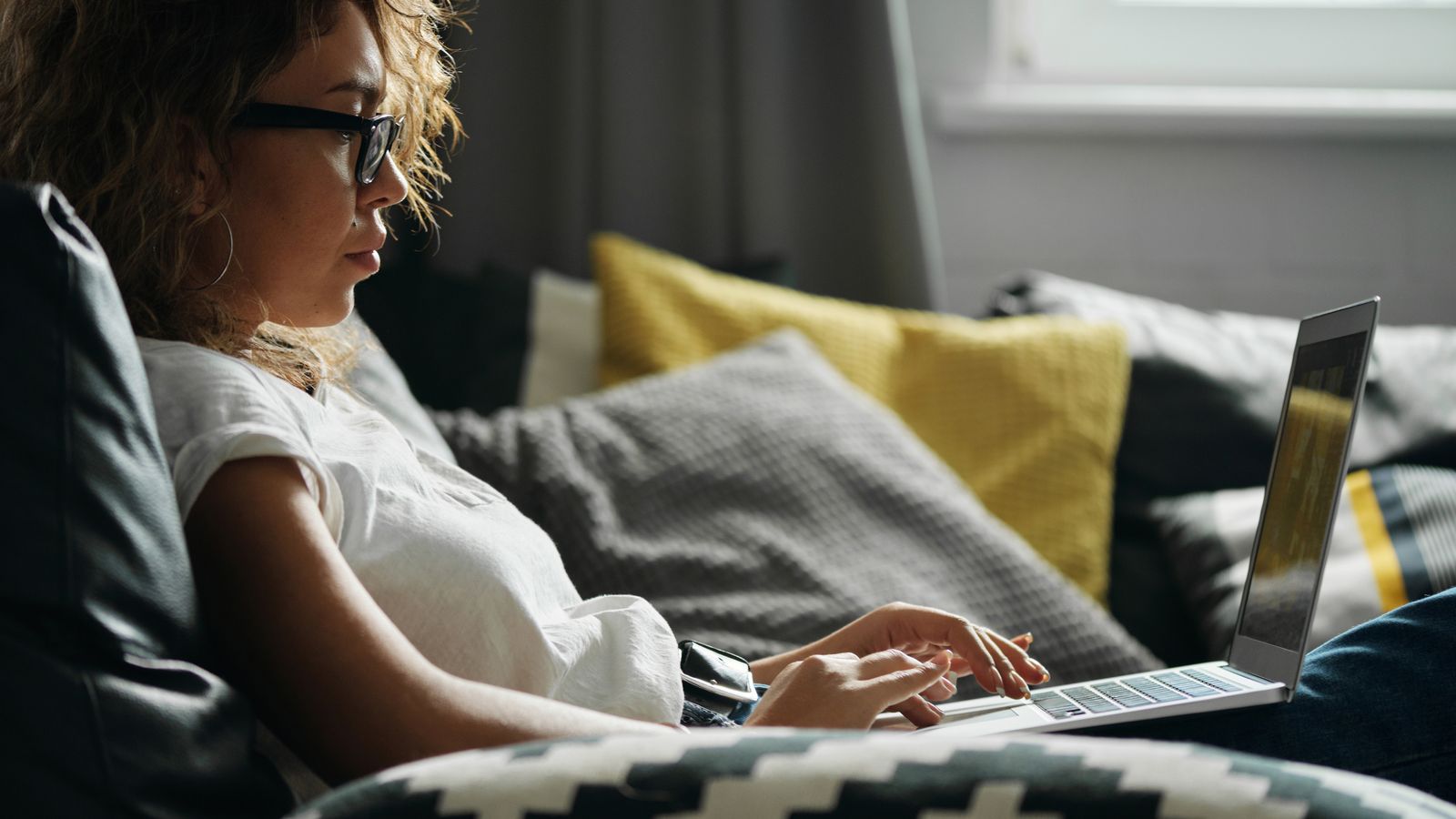 A woman building a virtual scrapbook page on her laptop at a sunlit desk at home